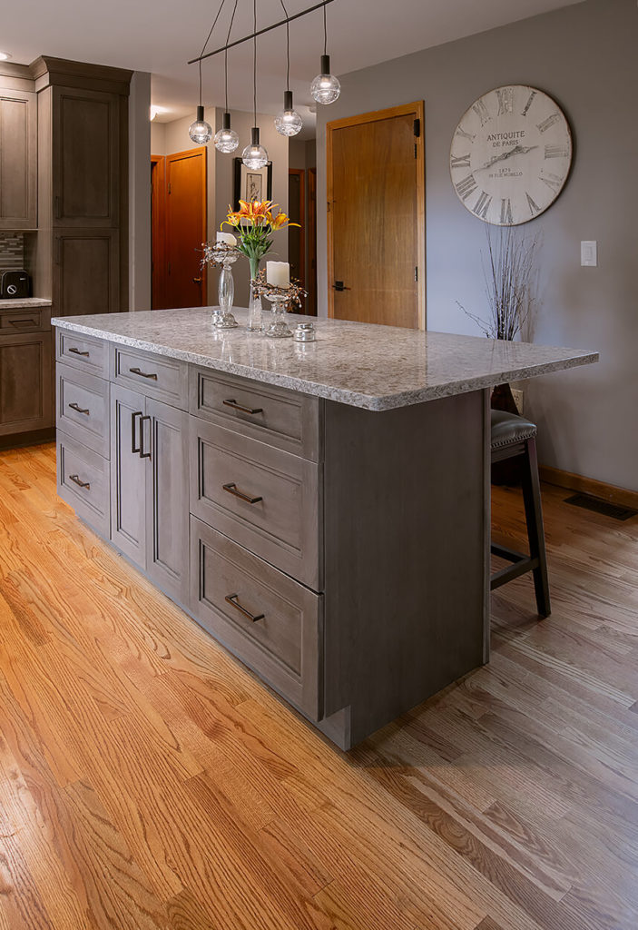 View of the Ultracraft island cabinets, Cherry Wood with Wicker Park door style and Coastal Grey stain finish, the eased edge on the Cambria New Quay quartz countertop.